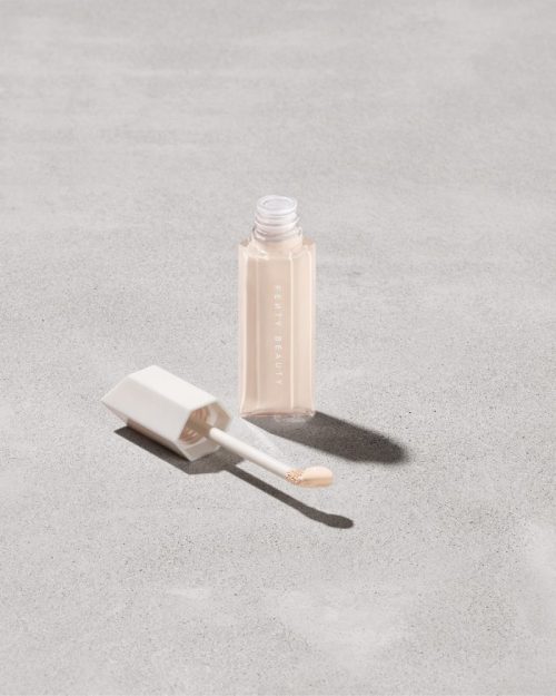 Open bottle of Fenty Beauty We're Even Hydrating Longwear Concealer with doe foot applicator in shade 100c on a concrete background.