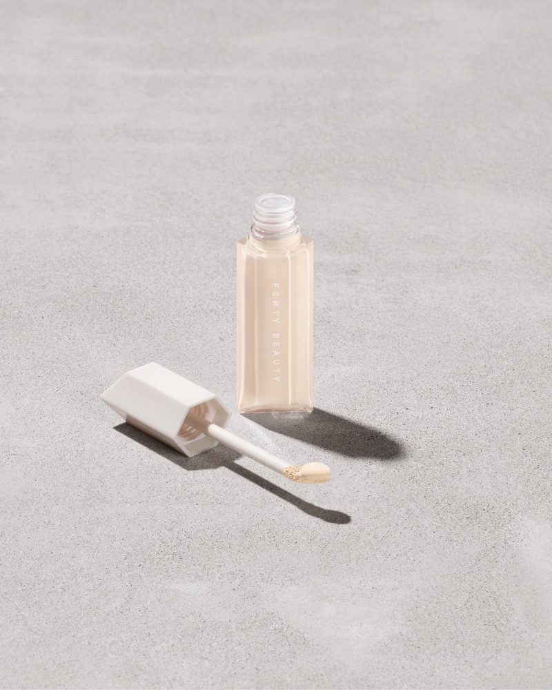 Open bottle of Fenty Beauty We're Even Hydrating Longwear Concealer with doe foot applicator in shade 110w on a concrete background.